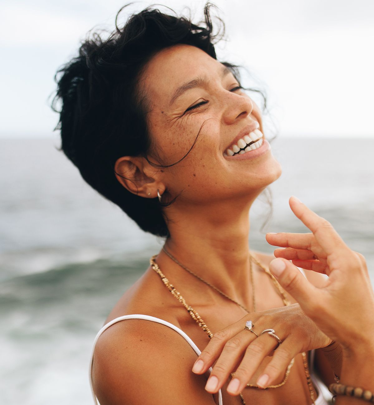 Smiling Eatontown med spa model near the ocean, wearing jewelry.